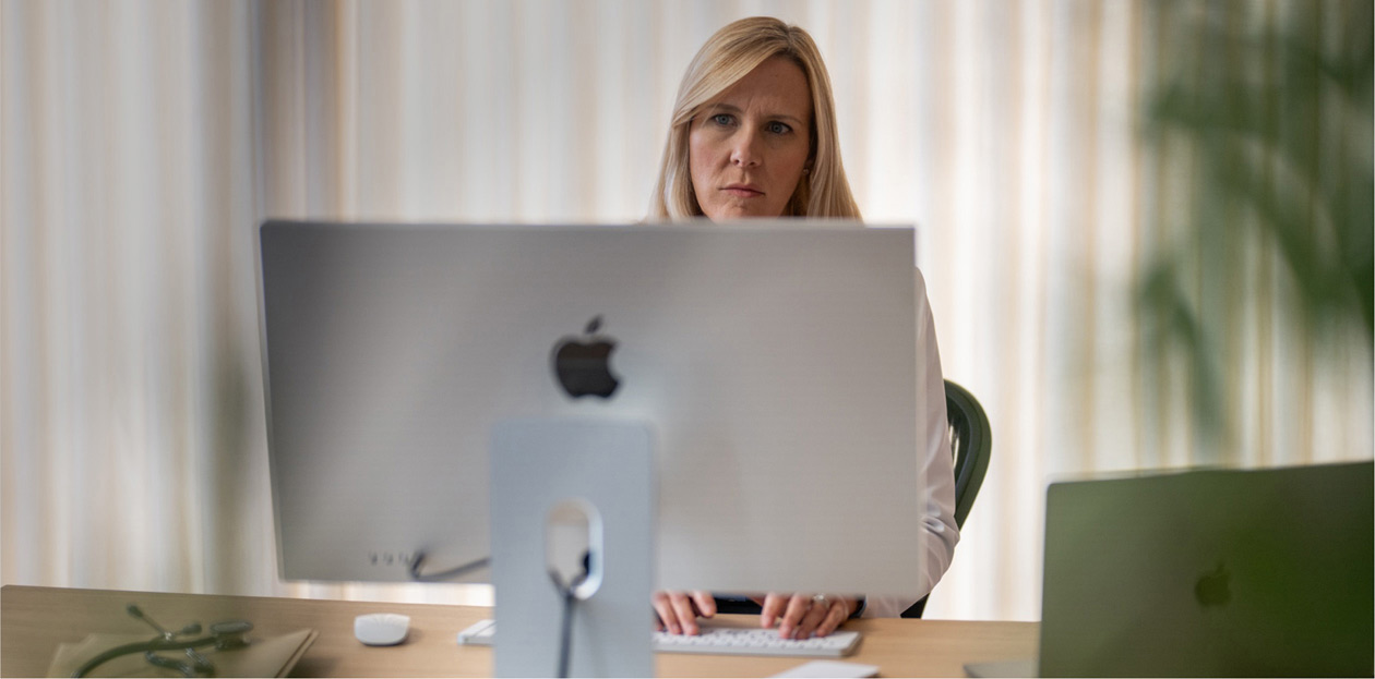 En helsearbeider ser på en iMac-skjerm ved skrivebordet sitt.