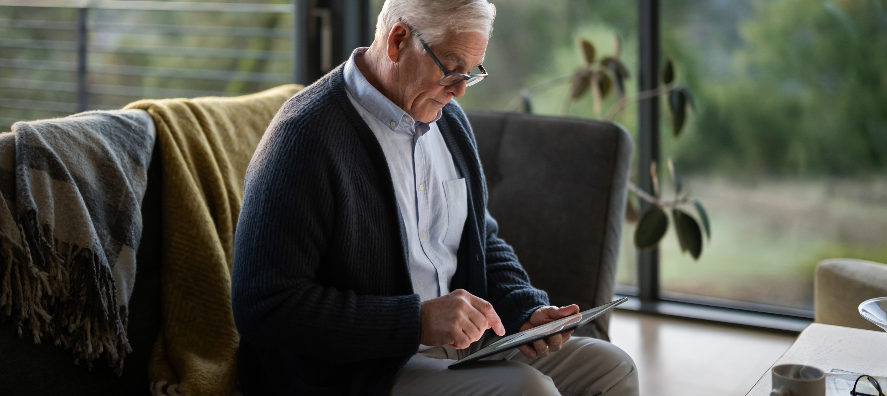 Un homme âgé assis sur un canapé consulte un iPad.
